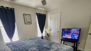 Une chambre à coucher avec un lit, un ventilateur de plafond, une télévision et une porte.
