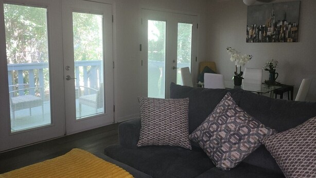 Un salon avec un canapé gris, des coussins à motifs, un plaid jaune et un tableau représentant un paysage urbain accroché au mur.