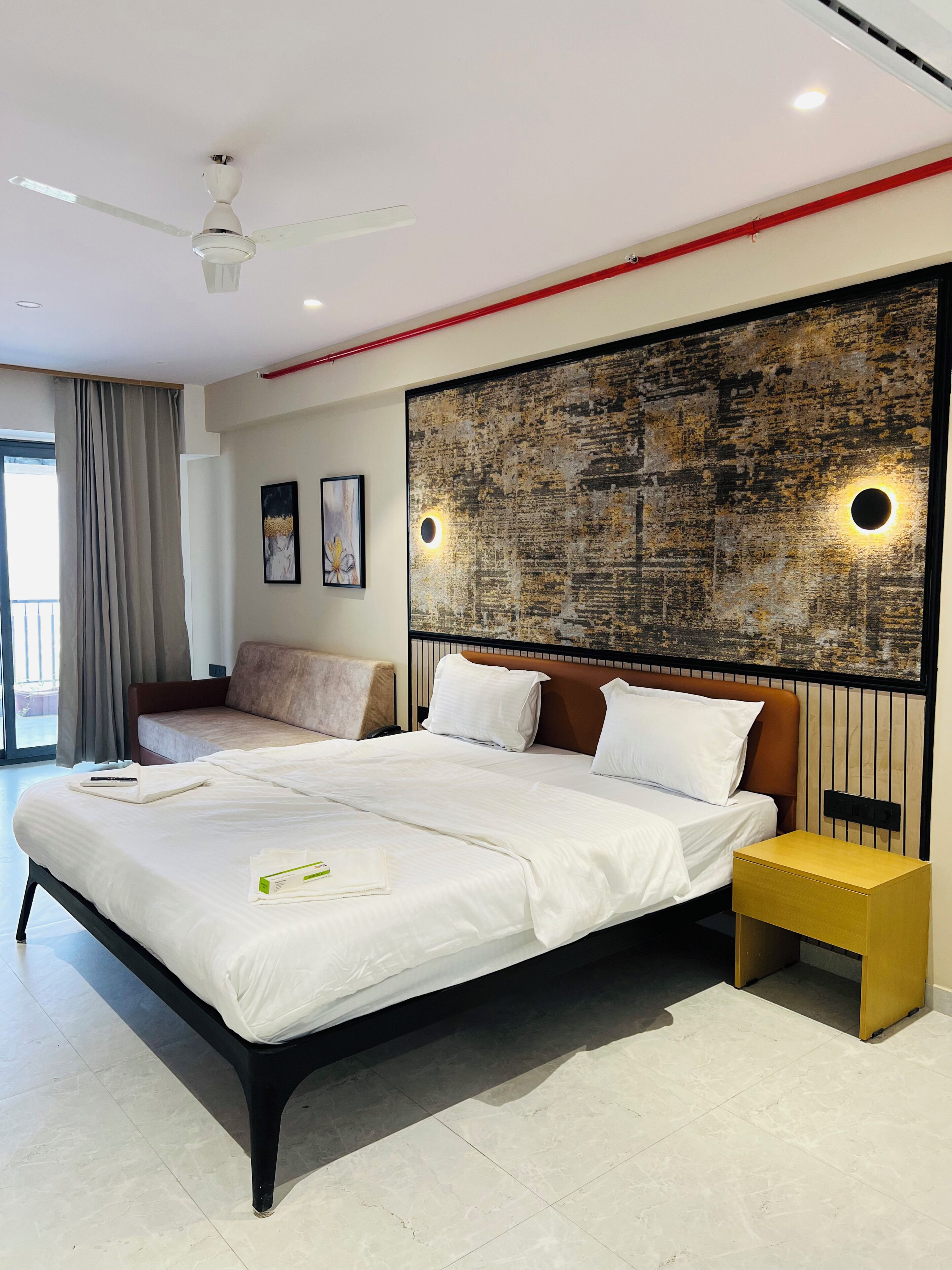 Habitación de hotel moderna con una cama grande, una mesita de noche, un ventilador de techo y vistas al exterior.