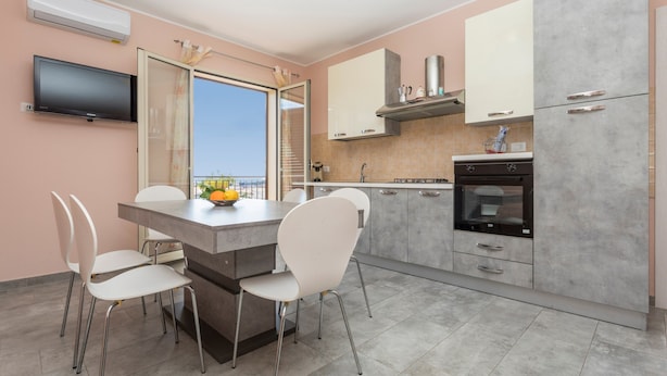 A modern kitchen with a dining area, a TV mounted on the wall, and a view through the glass door. - Villa Veronica – with Sea View (Mascali)