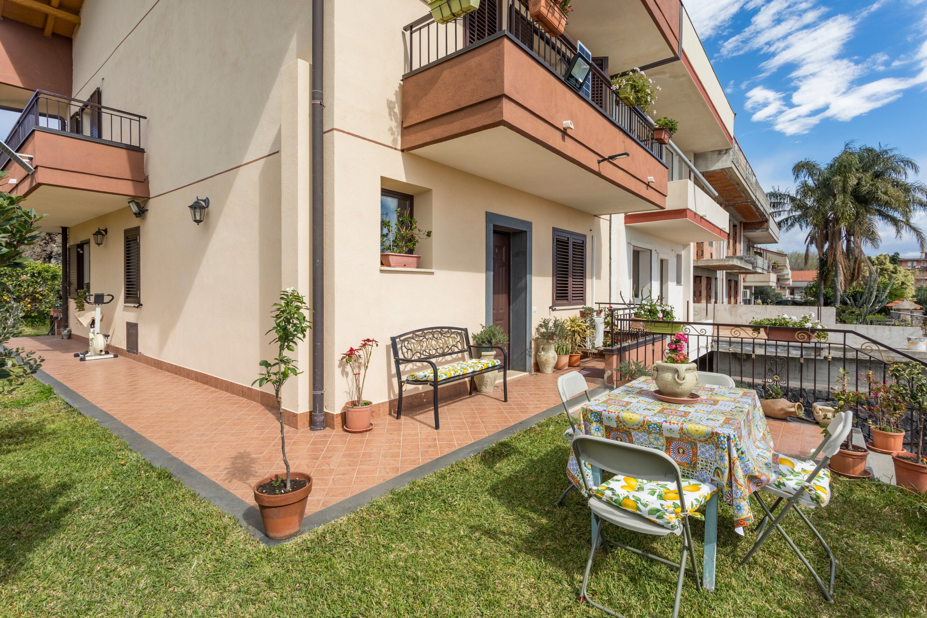 Un edificio residencial con balcón, plantas en macetas, una mesa con mantel y una silla.