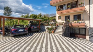 A two-story building with a covered parking area, a staircase, and potted plants. - Villa Veronica – with Sea View (Mascali)