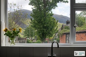 Une fenêtre donnant sur une montagne, un arbre et un bâtiment en briques.