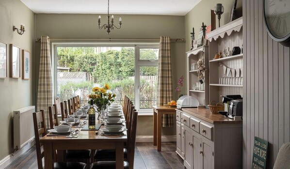 A dining room with a long table set for a meal, a chandelier, and a view of greenery outside.