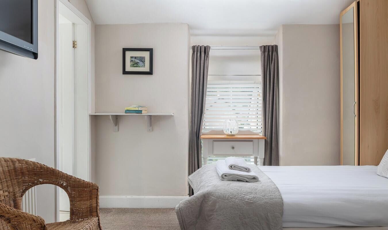 A bedroom with a bed, a chair, a shelf with books, a picture on the wall, and a window with curtains.