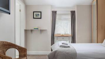 A bedroom with a bed, a chair, a shelf with books, a picture on the wall, and a window with curtains.