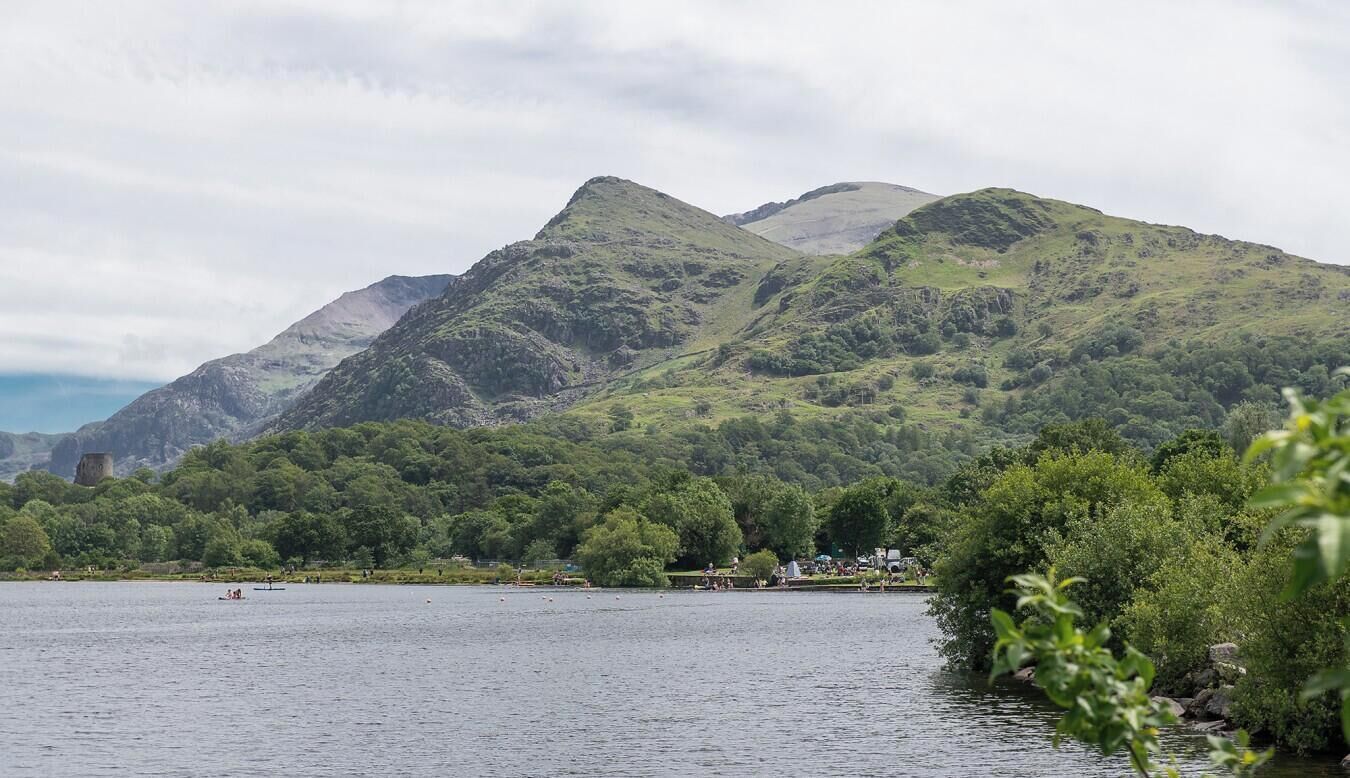 Ein See, umgeben von grüner Vegetation, mit Bergen im Hintergrund.