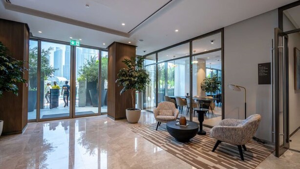 Un lobby moderno con puertas de vidrio, una mesa de centro, zona de estar y una planta en maceta.