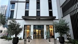 Un edificio moderno con entrada central, grandes ventanales y un camino pavimentado que conduce a la entrada.