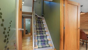 Una escalera con alfombra escocesa, barandillas de madera y una puerta que da a un cuarto con una mesa de comedor.