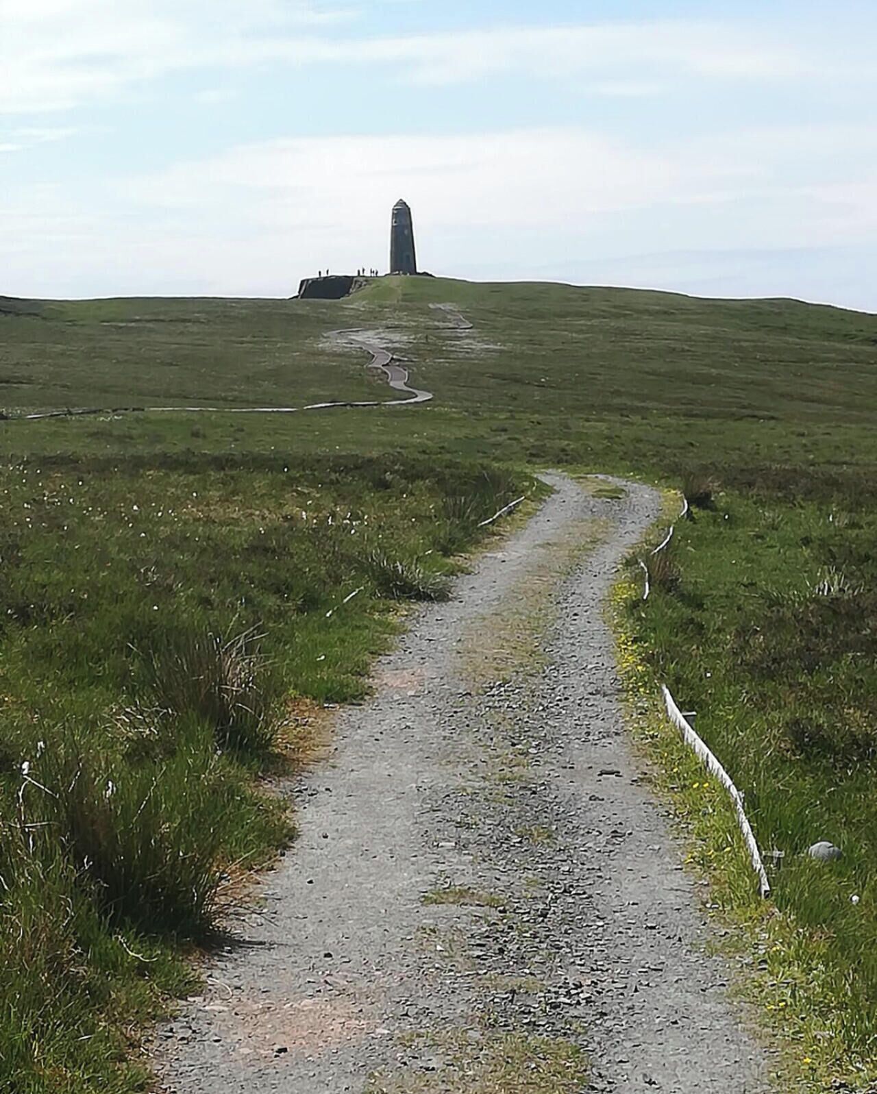 A gravel path leading to a tall, narrow structure on a grassy hill.