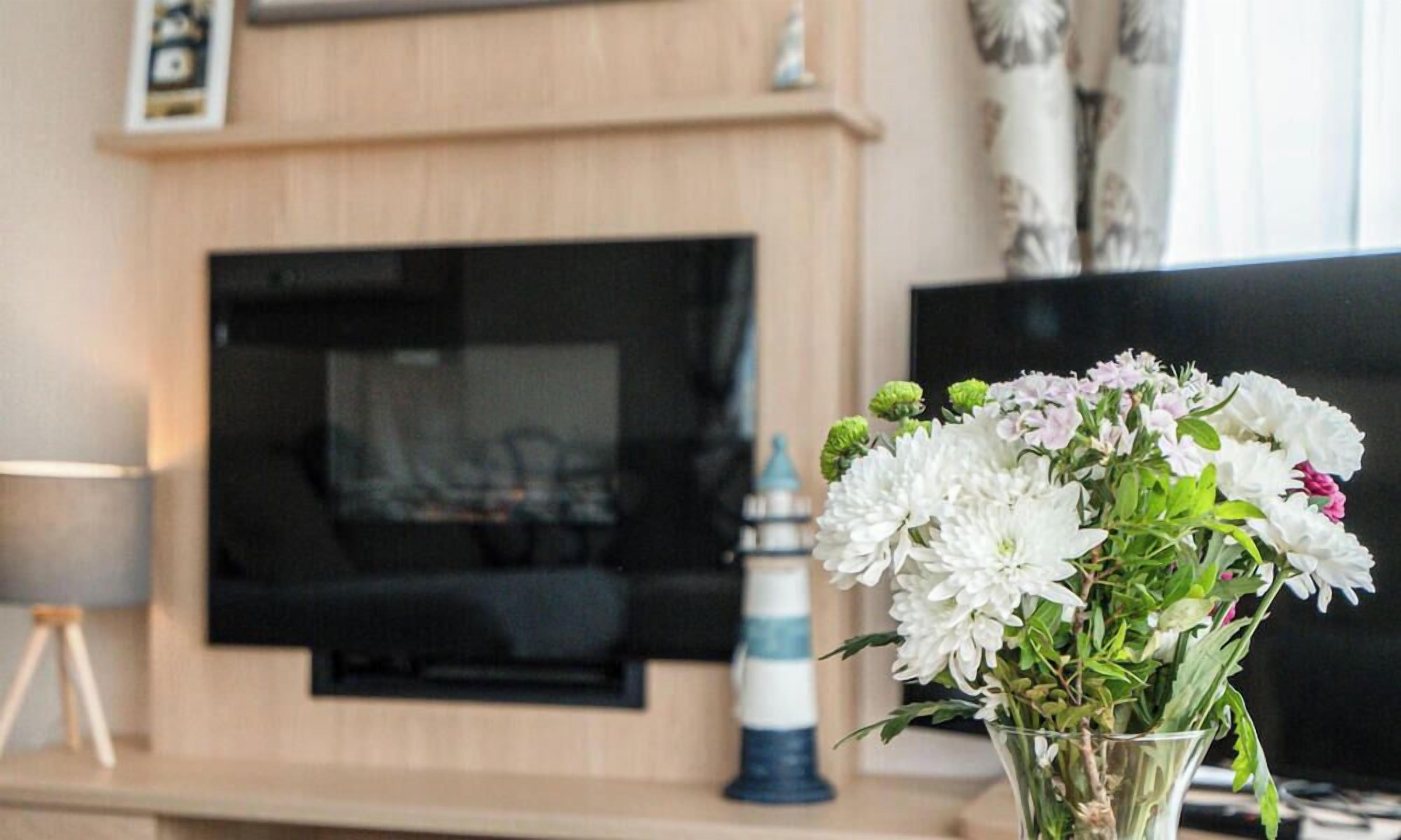 Ein Wohnzimmer mit Kamin, einem flachbildfernseher darüber und einer Blumenvase auf einem Tisch.