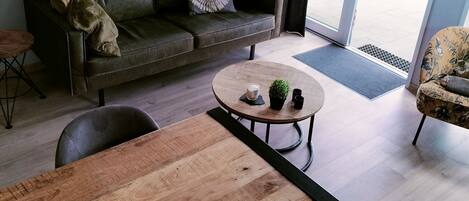 Ett modernt vardagsrum med en soffa, ett runt soffbord, ett matbord och ett stort fönster med gardiner.