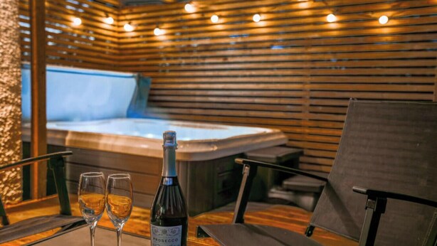 Een kamer met een houten lattenplafond, een jacuzzi en een fles wijn op een tafel.