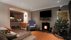 Een woonkamer met een open haard, een aan de muur bevestigde televisie, een kerstboom en een gezellige zithoek.