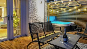 Een terras buiten met een bubbelbad, een tafel met een fles en glas, en een bank.