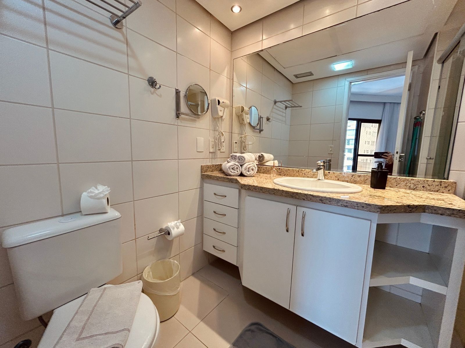 Une salle de bain moderne avec un lavabo blanc, un plan de toilette et des murs carrelés. On y trouve des toilettes, une serviette et une poubelle.
