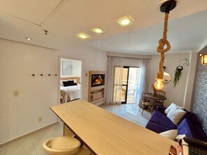 A modern living room with a sofa, a wooden table, and a TV. There is a balcony with a view. - SHB - Apê Retrô - Beira-Mar (Santos)