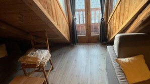 Ett sovrum på entresolplan med trägolv, en soffa, en bänk och utsikt genom en glasdörr.