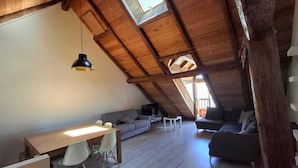 Ett rum i loftstil med ett träpanelat tak, ett matbord med stolar, en soffa och ett litet soffbord.