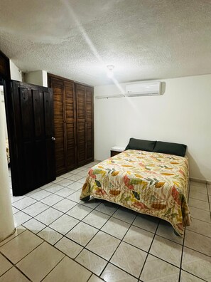 Une chambre à coucher comprenant un lit, une armoire, un sol carrelé et un appareil de climatisation.