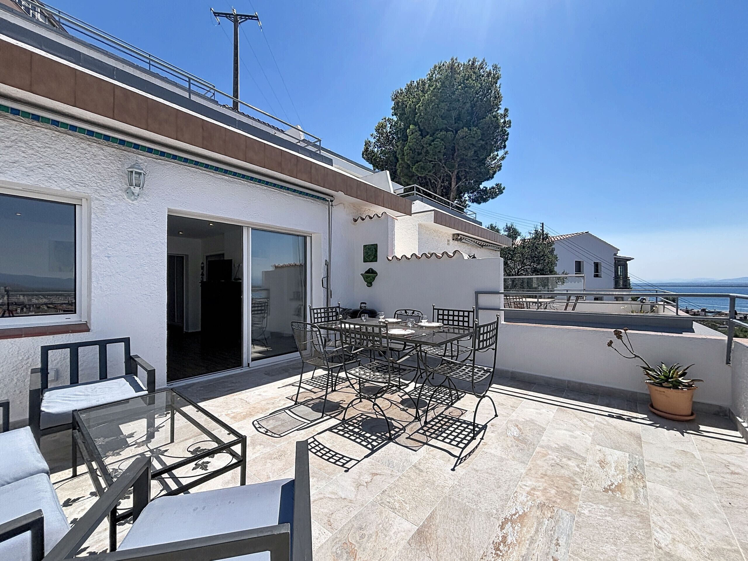 A rooftop terrace with outdoor seating, a view of the sea, and a building with a white facade.