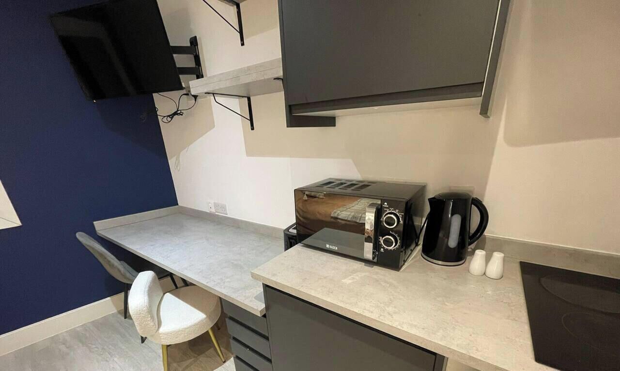 Una cocina compacta con microondas, tostadora, cafetera y un taburete pequeño.