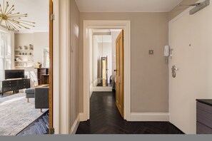 A hallway with a dark wood floor, white walls, and a door leading to a bathroom. - Punk Hip Plush 1-bed in Camden Town (London)