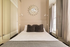 Een hotelkamer met een groot bed, twee wandlampen, een spiegel met zonnestralenmotief en een raam met gordijnen.
