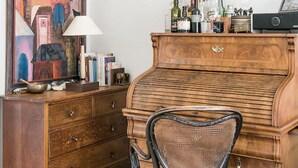 Una habitación con un piano de madera, una silla de mimbre, un aparador de madera y un cuadro en la pared.