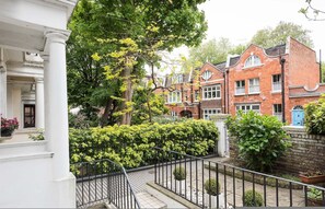 A row of red brick houses with white trim, a white building with columns, and a black metal fence. - The Hummingbird 1 Bedroom by Kensington Gardens (London)