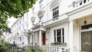 Una hilera de casas urbanas blancas con balcones, una puerta roja y una cerca de metal negro.