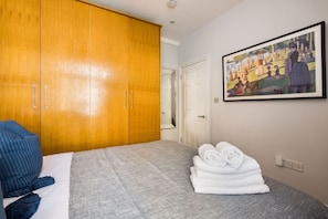 Ein Schlafzimmer mit einem Bett, einem Holzschrank, einem Bild an der Wand und einem gefalteten Handtuch auf dem Bett.