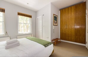 A bedroom with a bed, a wardrobe, a window, and a door. - London Is Yours - 2 Bedroom in Kensington (London)