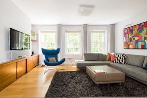 A modern living room with a flat-screen TV, a blue chair, a grey sofa, and a black rug. - London Is Yours - 2 Bedroom in Kensington (London)