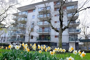 A modern apartment building with multiple balconies, a tree in the foreground, and a black metal fence. - Great Value 1-bedroom Near Tower Bridge (London)