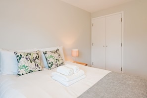 A neatly made bed with white linens and a grey throw blanket, two floral-patterned pillows, a bedside lamp, and a closed door. - Great Value 1-bedroom Near Tower Bridge (London)