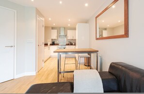 A modern kitchen with white cabinets, a wooden table, and two bar stools. - Great Value 1-bedroom Near Tower Bridge (London)