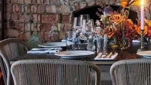 A dining area with a brick wall, wicker chairs, and a table set with glassware and flowers. - Victorian Blush 1BR Near Portobello Notting Hill (London)