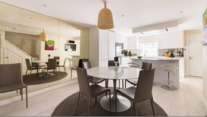 Une cuisine moderne avec des meubles blancs, un coin repas doté d’une table ronde et de chaises, et un escalier menant à un autre niveau.