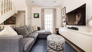 Un salon avec un canapé gris, un pouf et un téléviseur à écran plat fixé au mur.