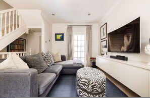 Ein Wohnzimmer mit grauem Sofa, Ottoman und einem an der Wand montierten Flachbildfernseher.