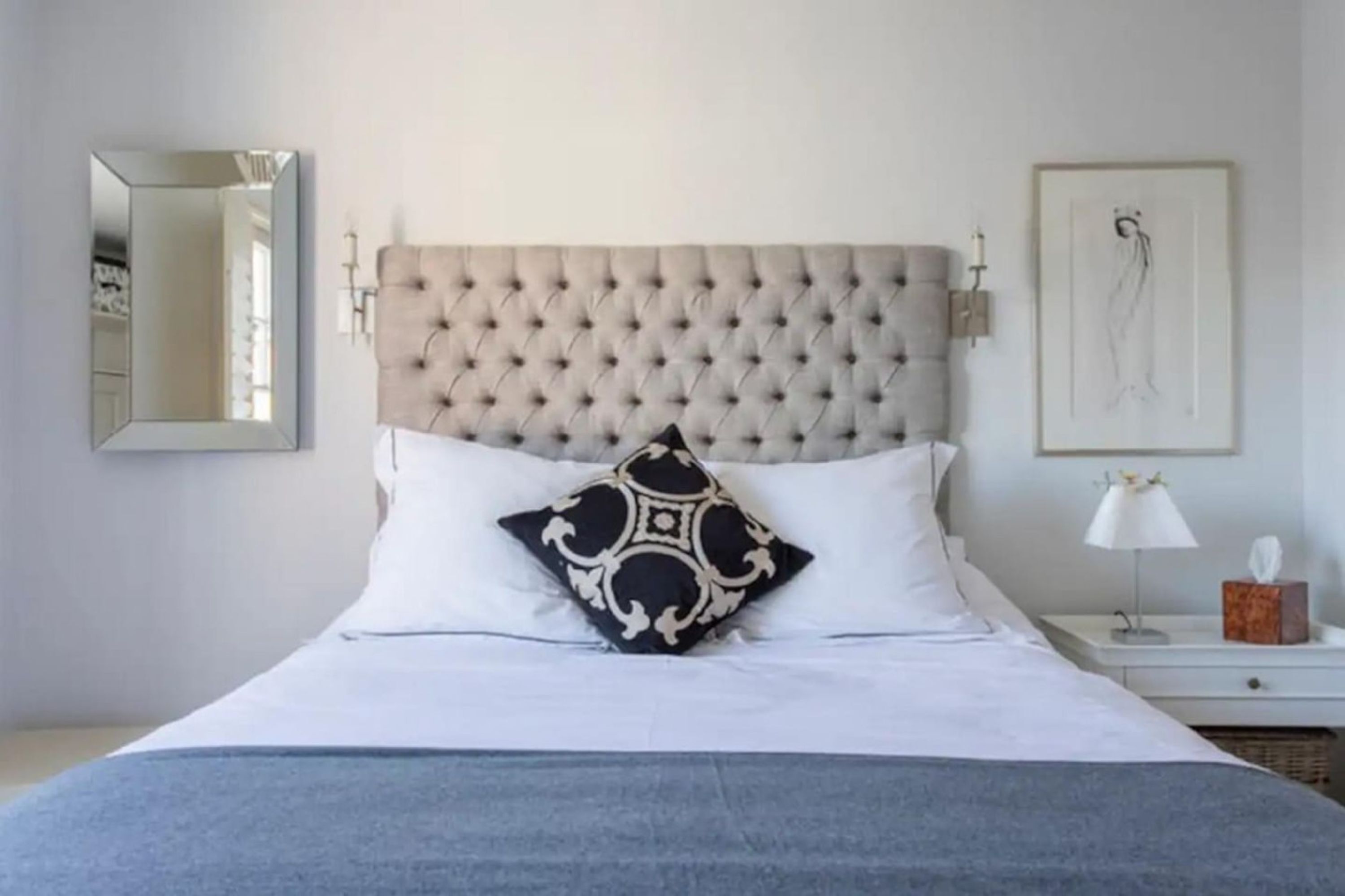 A neatly made bed with a tufted headboard, a bedside table with a lamp, and a framed artwork on the wall.