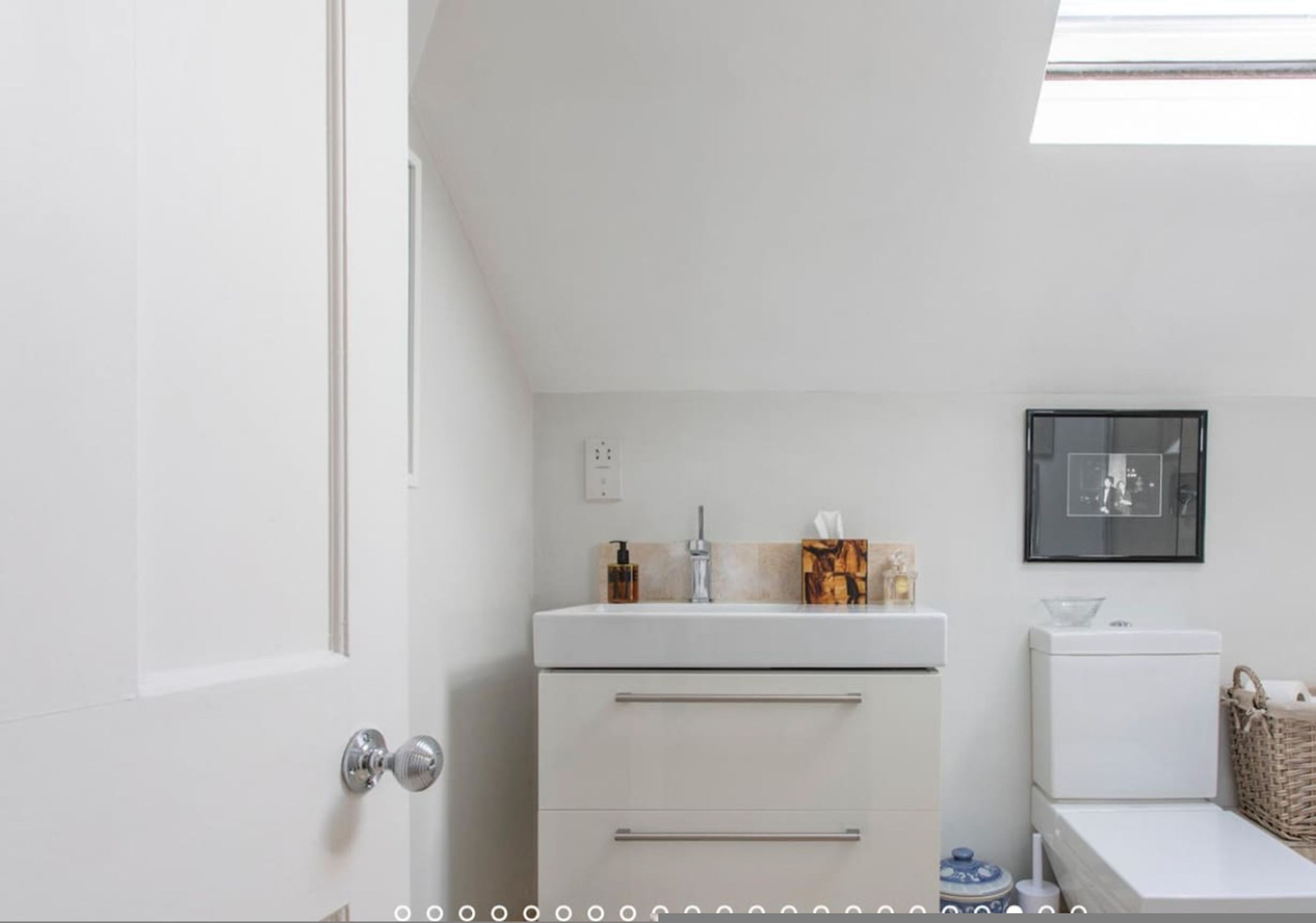 Une salle de bain blanche avec des toilettes, un lavabo et un tableau encadré au mur.