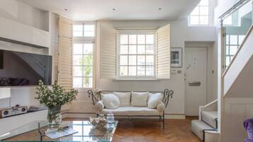 A living room with a sofa, a glass coffee table, a TV, and a staircase.