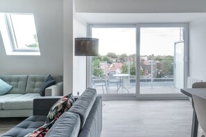 A modern living room with a sofa, a dining table, and a large sliding glass door leading to an outdoor area with a view of the city. - Newly Refurbished 2 bed With Fantastic View (London)