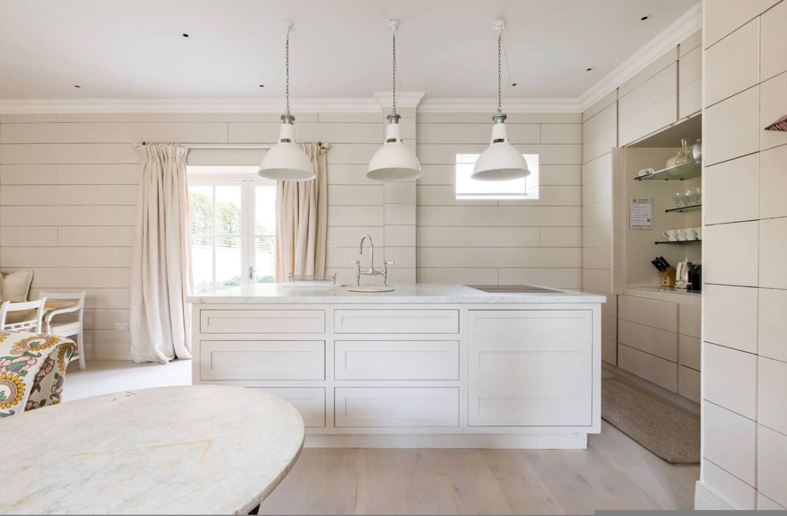 A kitchen with a central island, pendant lights, a window, and a dining area with a table and chairs.