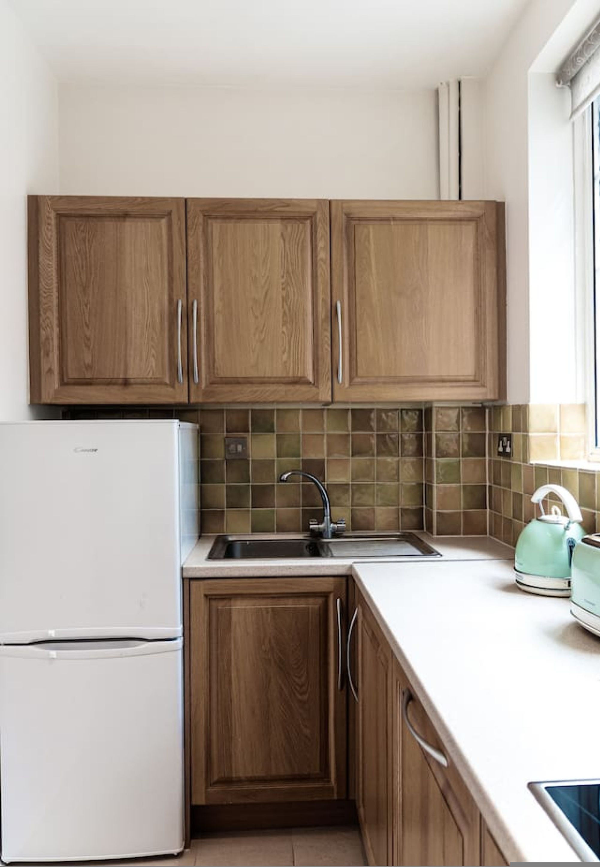 A kitchen with wooden cabinets, a white refrigerator, a tiled backsplash, and a kettle on the counter.