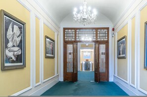 A hallway with a chandelier, wooden doors, and framed artwork on the walls. - Chestnut Blossom 1 Bedroom in Kensington (London)