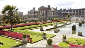 A formal garden with a fountain, neatly trimmed hedges, and a large building in the background. - The Bengal Tiger 2 BR With Patio in Notting Hill (London)